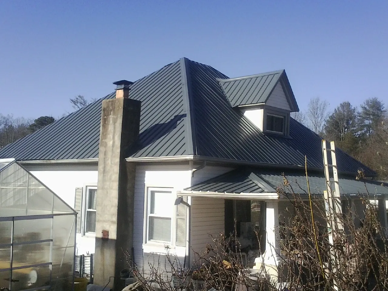 Dark blue standing seam metal roof on a white farmhouse with dormer — Slate & Tile Roof Repair by Roofing Brothers in Jellico