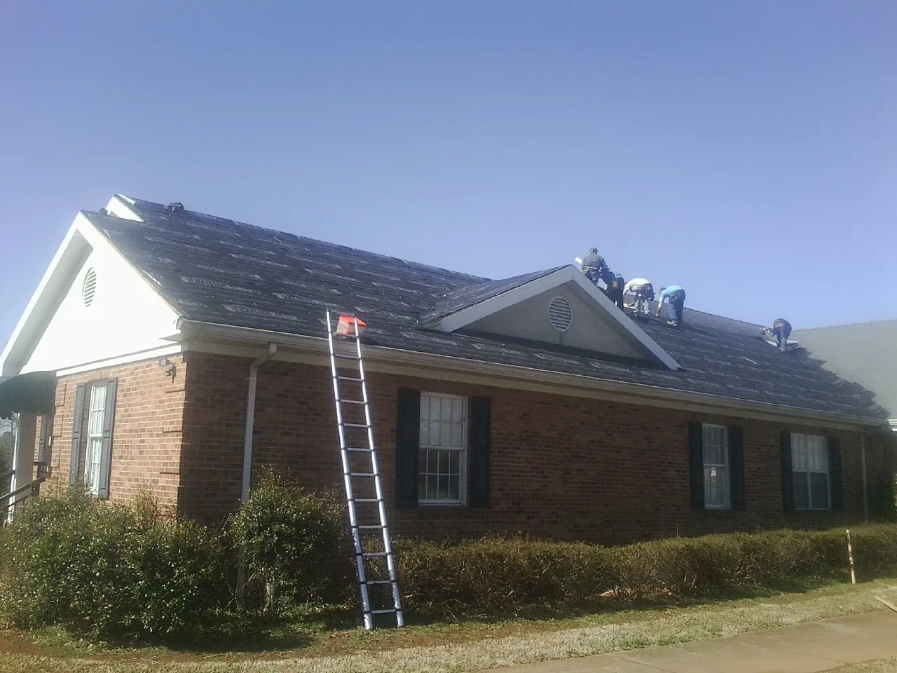 Crew tearing shingles off a brick ranch roof with a ladder set — Metal Roof Repair work by our crew in Jellico