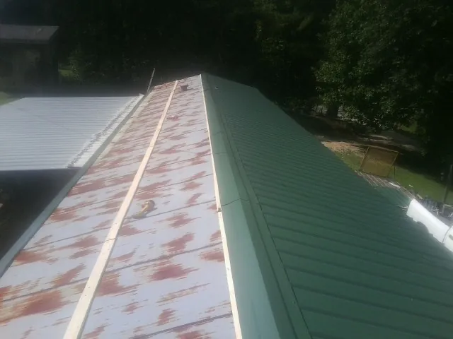 Old rusted panels beside newly installed green metal roofing — Wind Damage Roof Repair by Roofing Brothers in Jellico