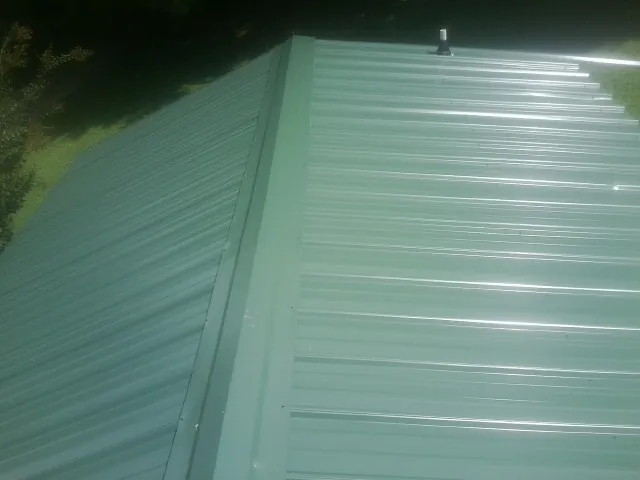 New green metal panels meeting at the ridge of a roof — Flat Roof Repair work by our crew in Jellico