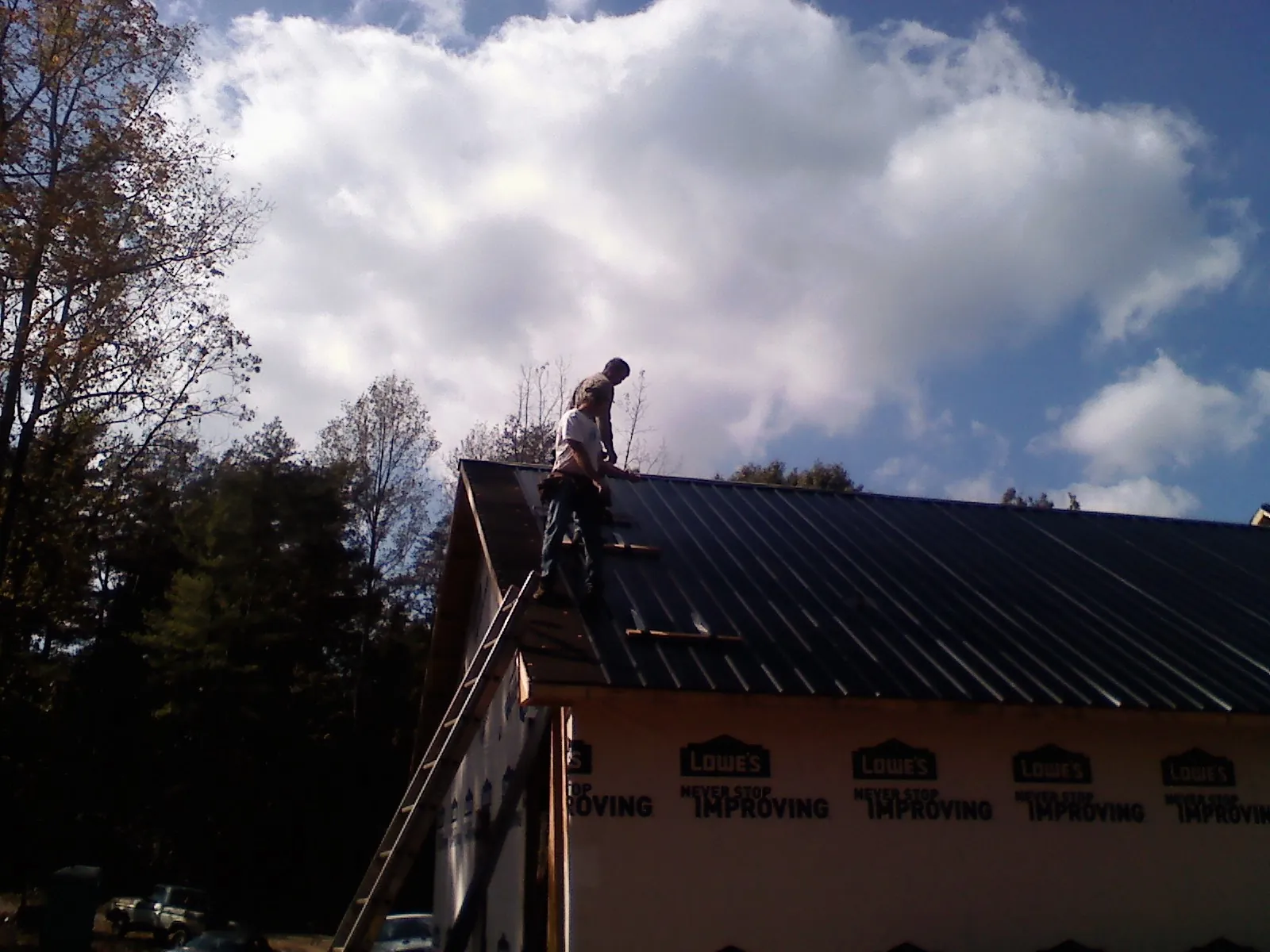 Roofer fastening dark metal panels high against a cloudy sky, from a Roof Inspection job in Jellico