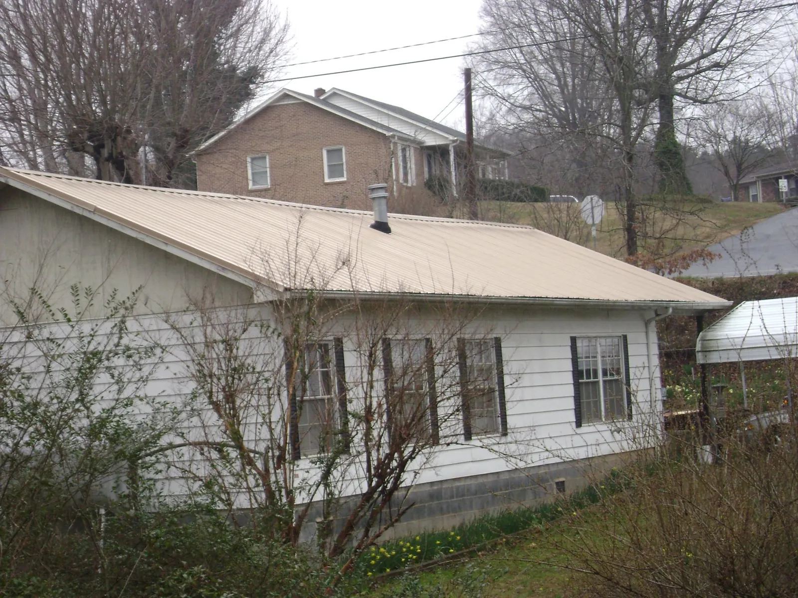Tan metal roof on a white sided house set into a hillside — Commercial Roofing by Roofing Brothers in Jellico