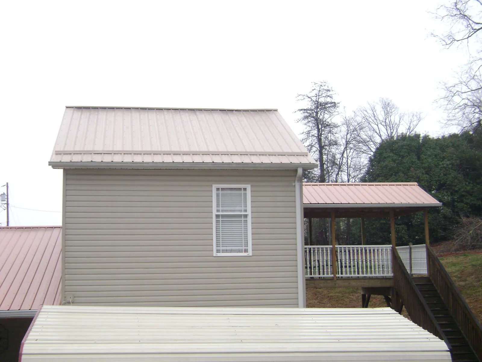 Tan metal roofs on a two story addition and attached porch, from a Roof Replacement job in Jellico